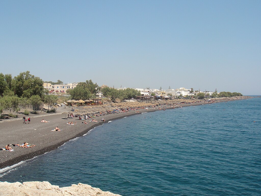 Kamari Beach in Santorini, featuring a sandy shoreline with calm water conditions, certified with Blue Flag status for environmental quality